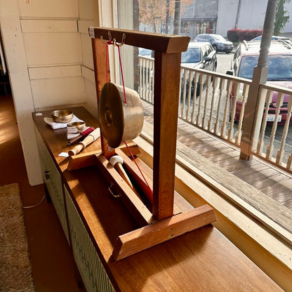 Wooden gong stand with gongs on a wooden surface near a window.