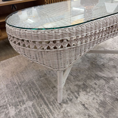 Wicker coffee table with glass top on a gray carpeted floor