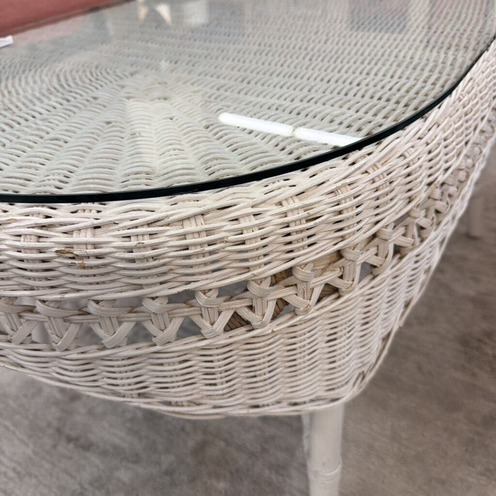 Round wicker table with a glass top on a gray floor.