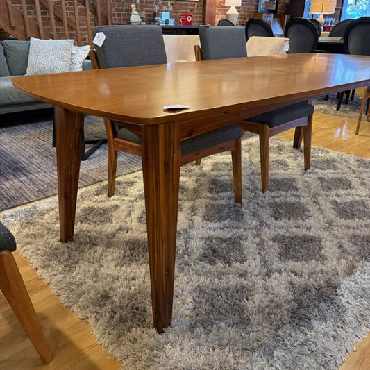 Wooden dining table with chairs on a patterned rug in a room setting.