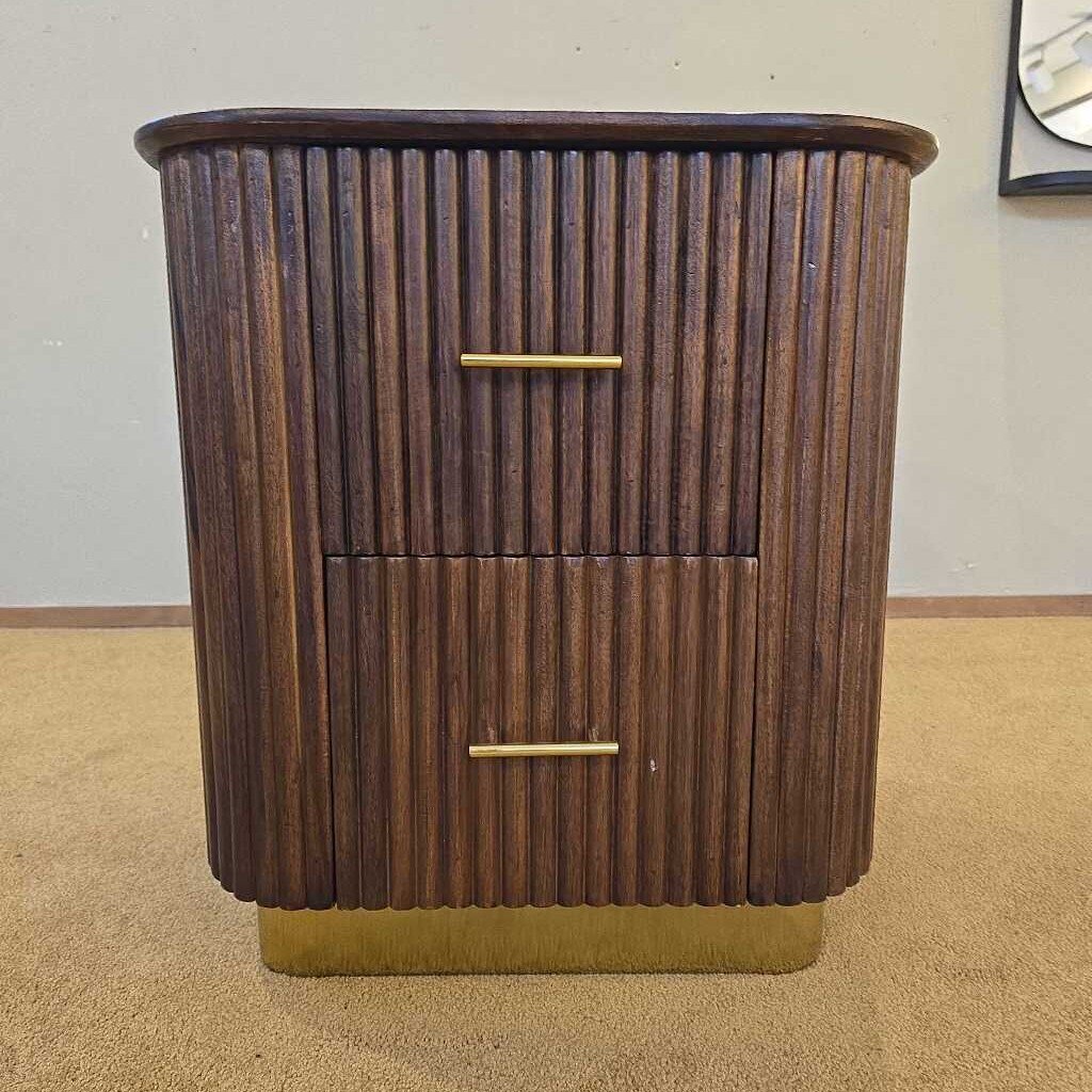 Wooden side table with two drawers and a gold handle on a beige carpet.