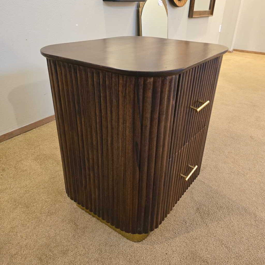Wooden side table with a ribbed design on a carpeted floor.
