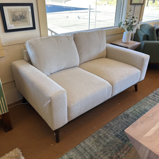 Beige sofa in a living room setting with a rug and window in the background