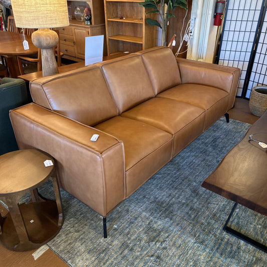 Brown leather sectional sofa in a showroom setting with furniture and decor around.