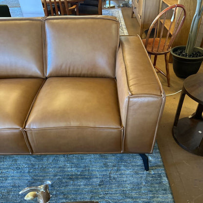Brown leather sofa in a room with wooden chairs and a blue rug.