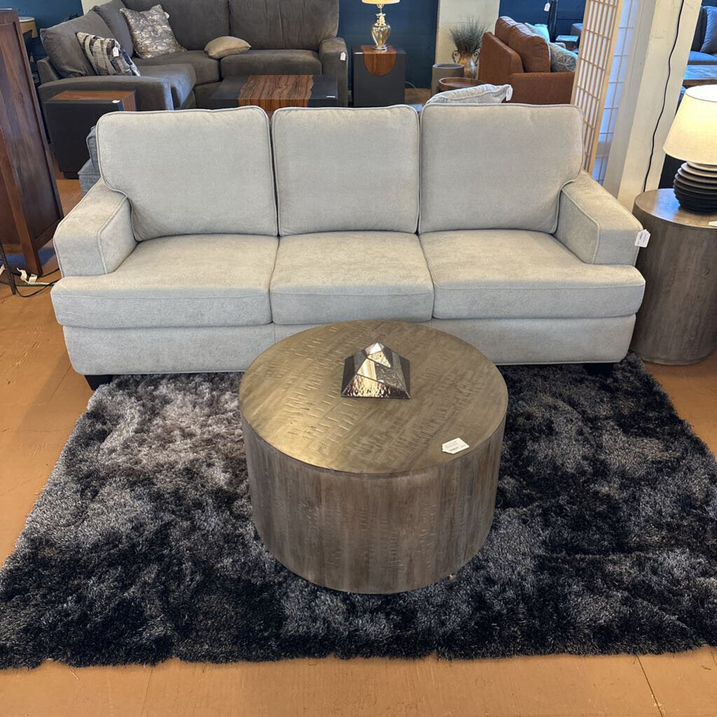Gray sofa with a wooden coffee table on a dark rug in a room setting.