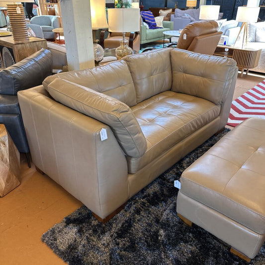 Beige leather sofa in a showroom setting with other furniture.