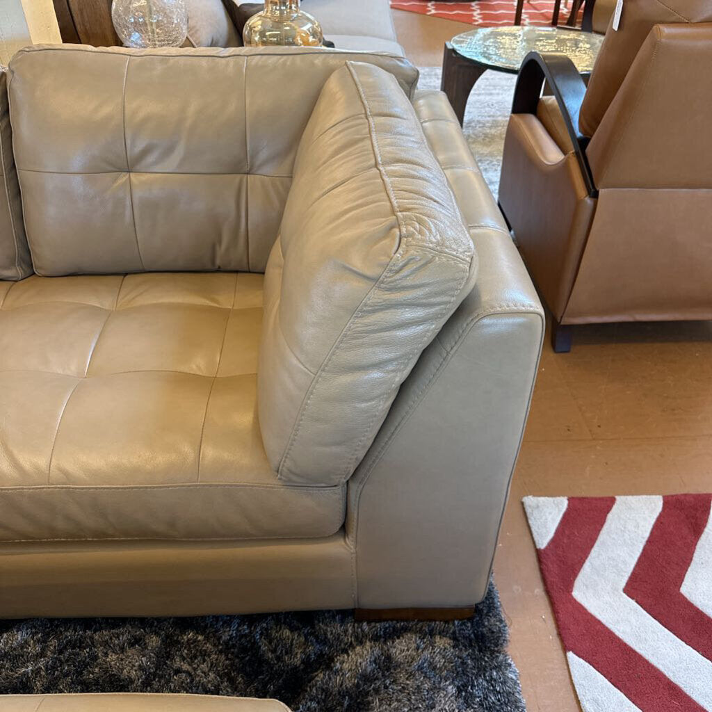 Beige leather sectional sofa in a living room setting with a rug and chair.
