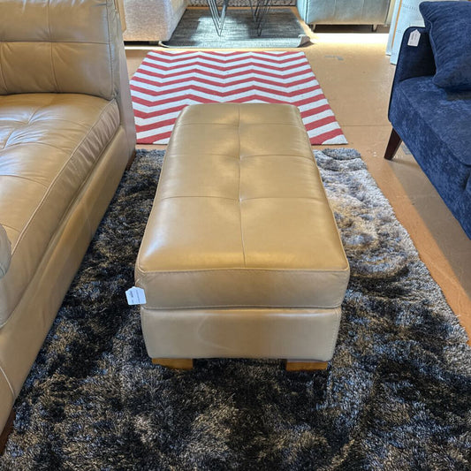 Beige leather ottoman on a patterned rug with a striped rug in the background