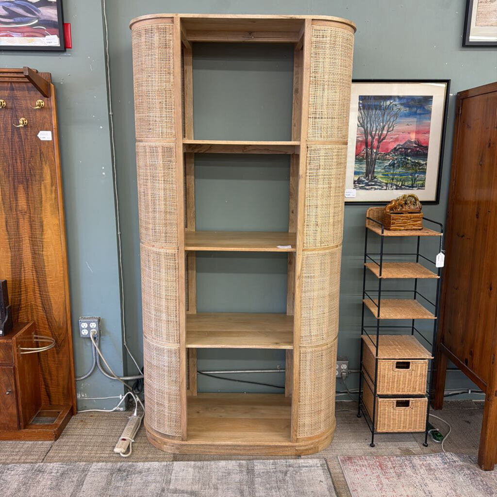 Tall wooden bookshelf with wicker accents in a room with other furniture and decor.