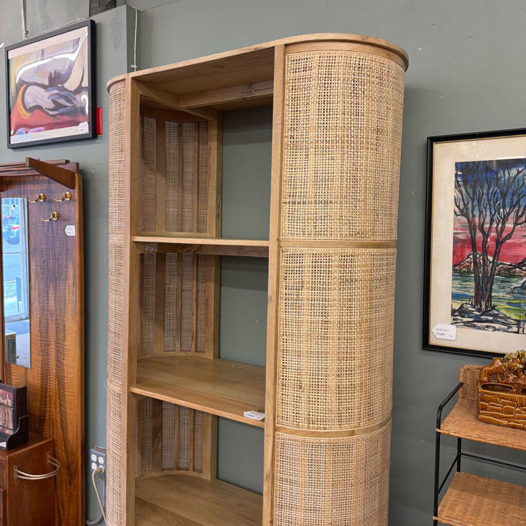 Wooden bookshelf with wicker design against a gray wall with framed artwork.
