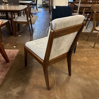 Wooden chair with gray cushion on a brown floor in a furniture store.
