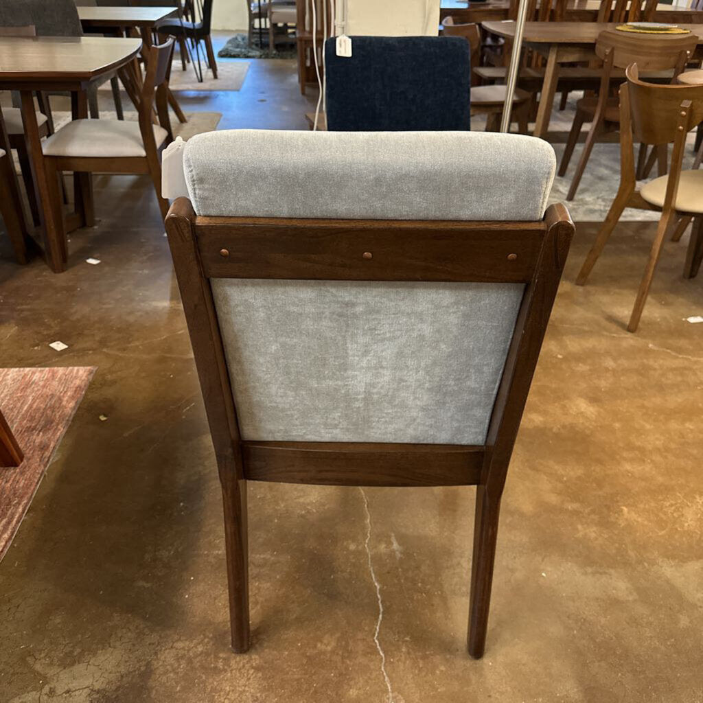 Wooden chair with gray cushion on a concrete floor in a warehouse setting