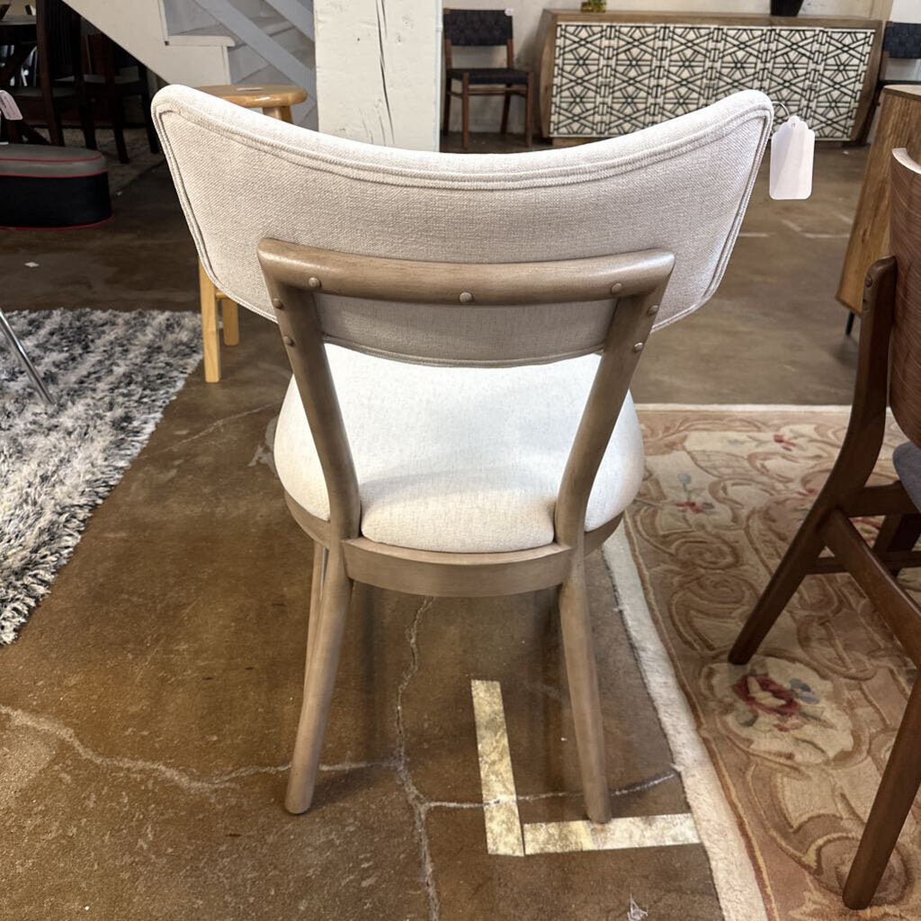Dining chair with beige cushioned backrest and seat in a room setting.