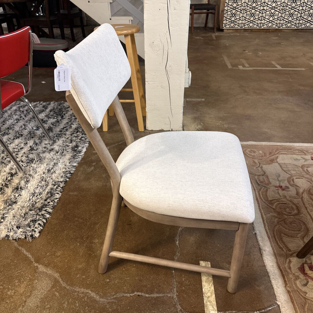 White cushioned chair on a brown floor with a red chair and patterned rug in the background.