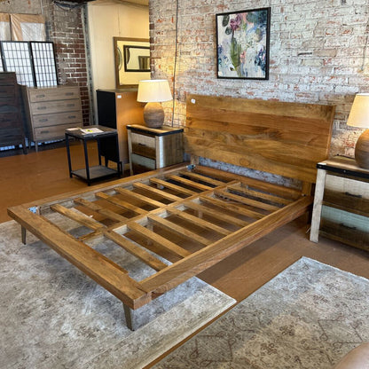 Wooden bed frame in a room with brick walls and furniture.