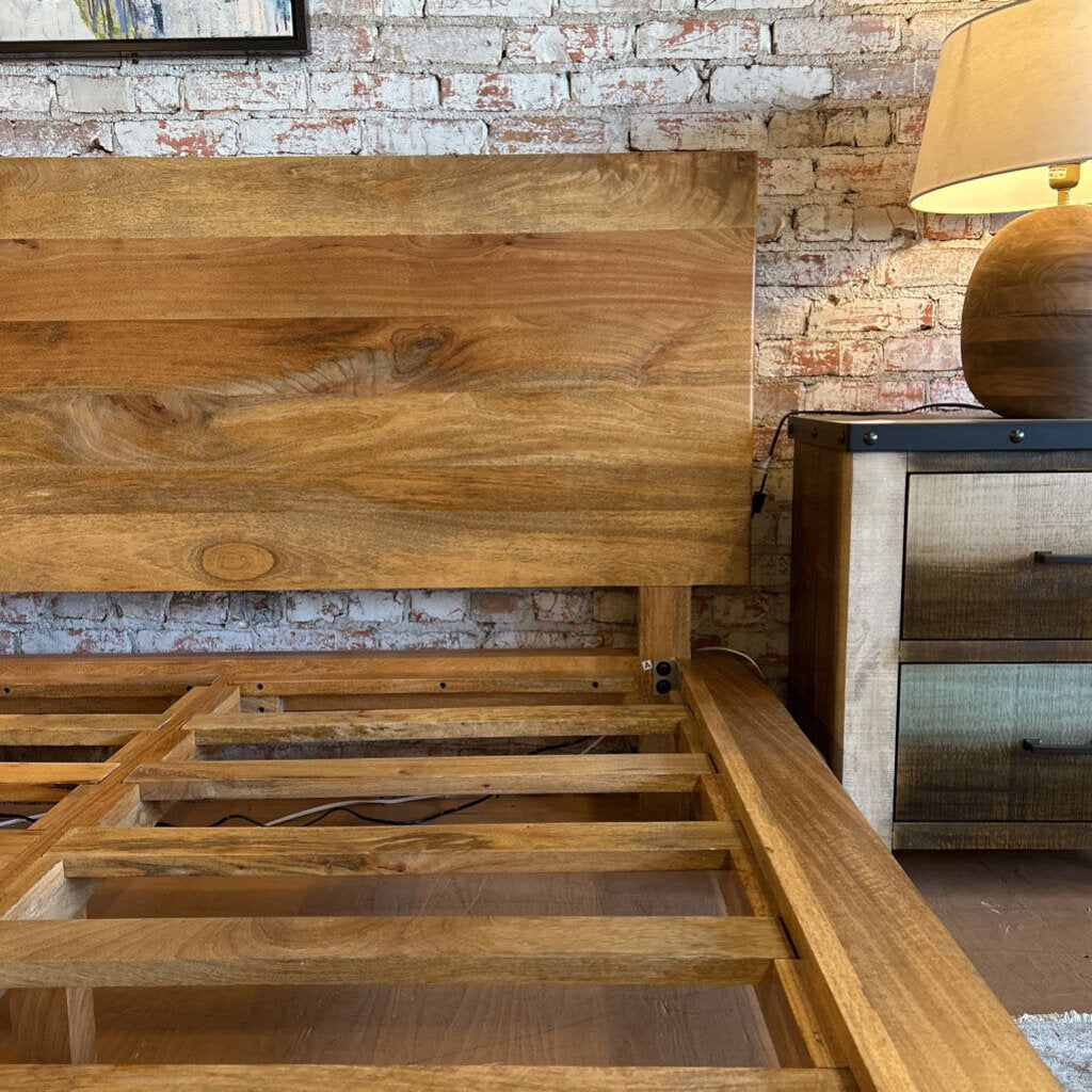 Wooden bed frame against a brick wall with a lamp on a nightstand.