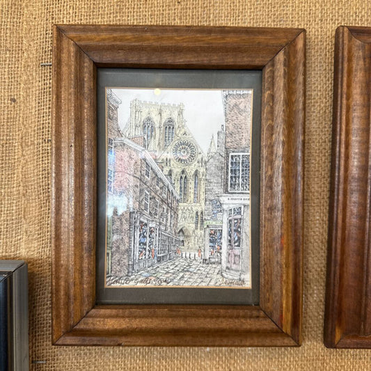 Framed artwork of a cityscape with a clock tower on a textured wall.