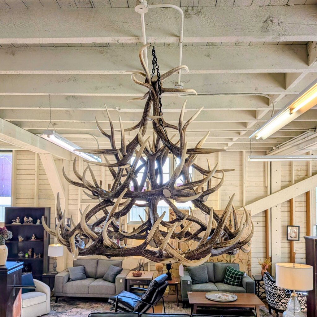 Large antler chandelier hanging in a living room with furniture and decor.