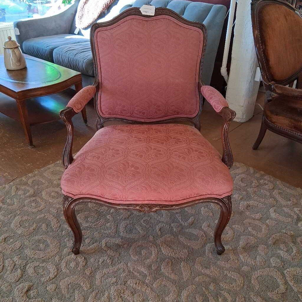 Pink upholstered chair in a room with a couch and coffee table.