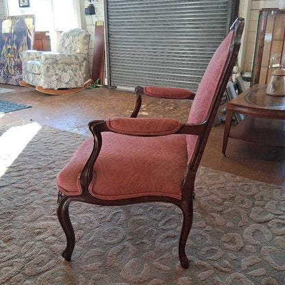 Vintage armchair with pink upholstery in a room with patterned carpet and other furniture.