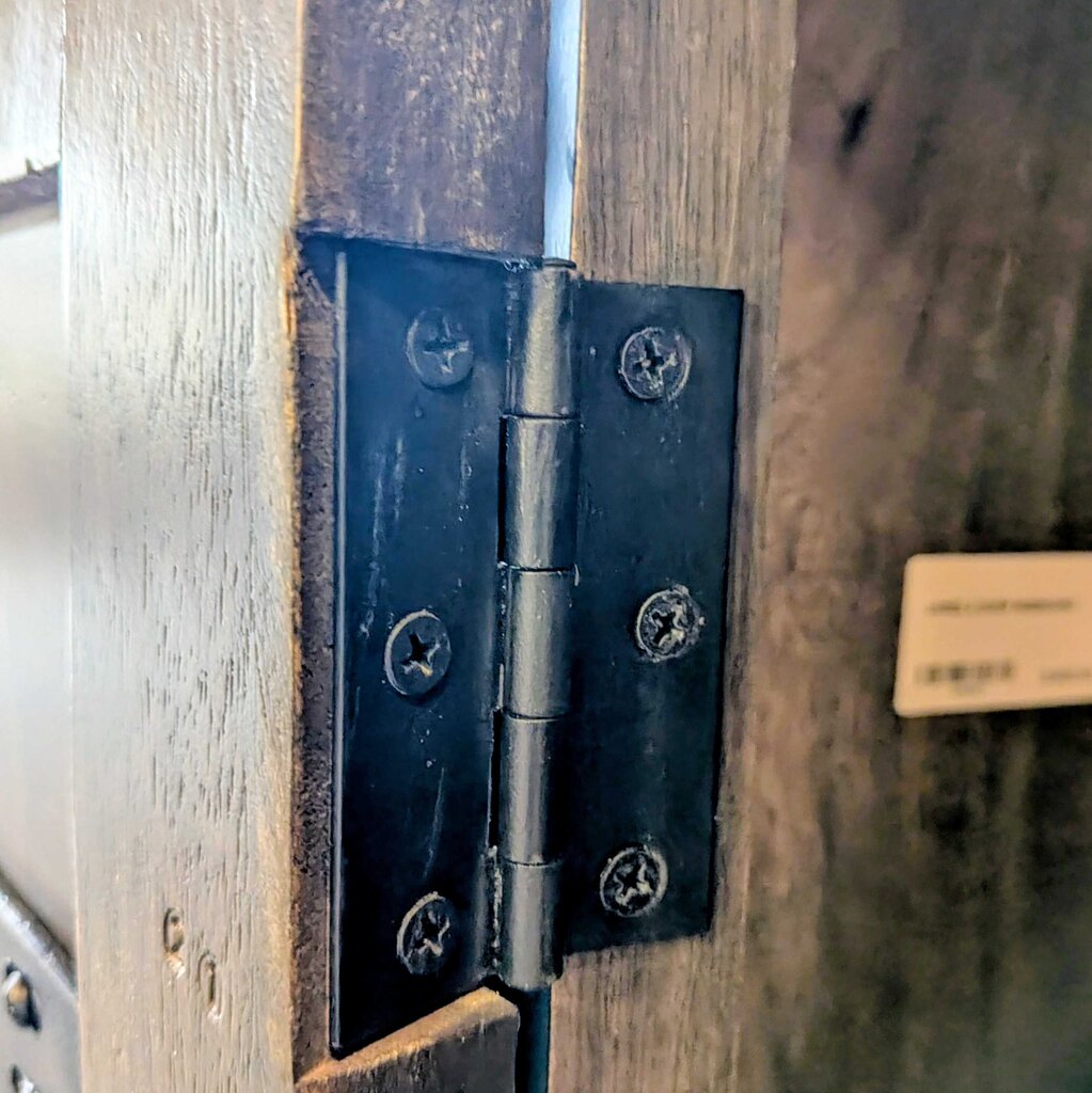 Close-up of a black metal hinge on wooden doors.