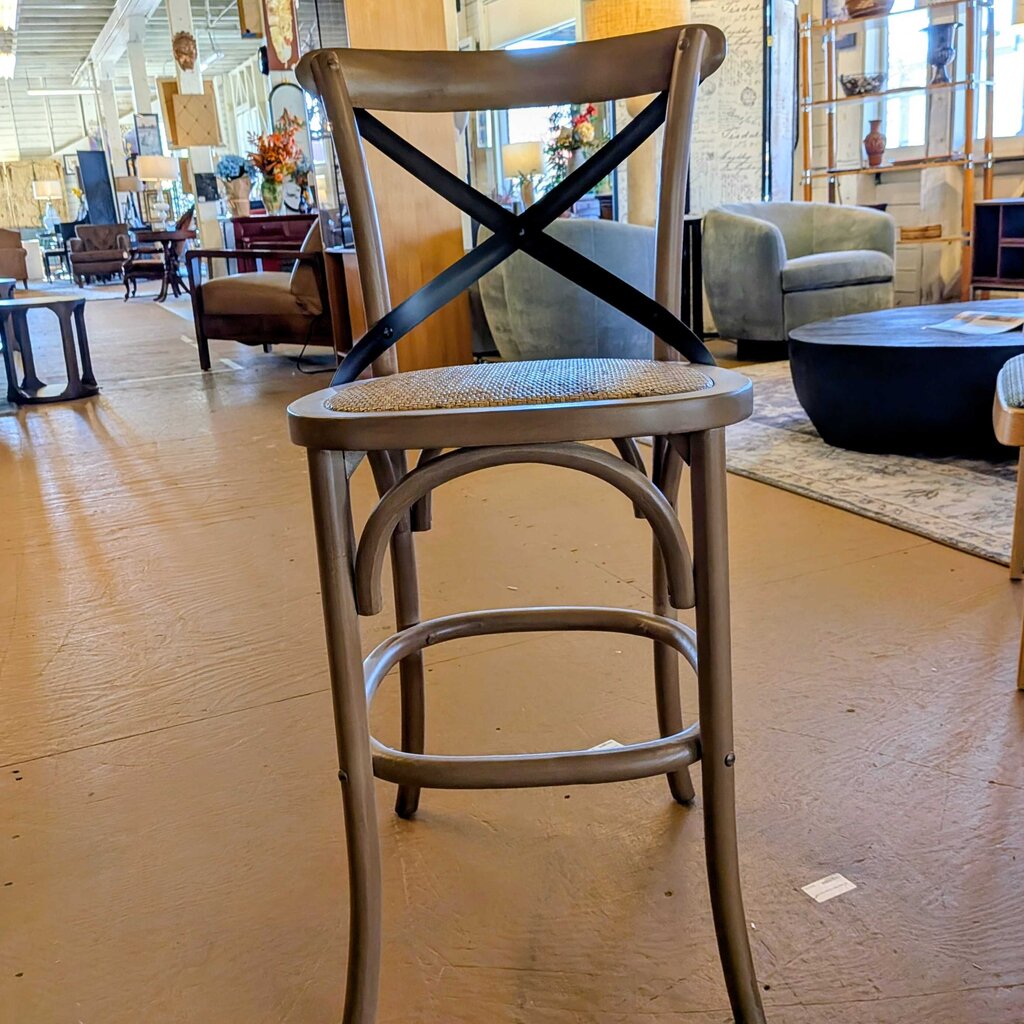 Wooden bar stool with a cross-back design in a showroom setting.