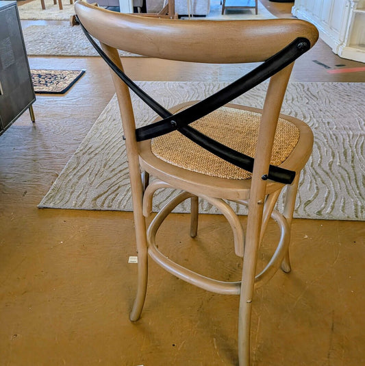 Wooden chair with a woven seat and black metal cross brace on a wooden floor.