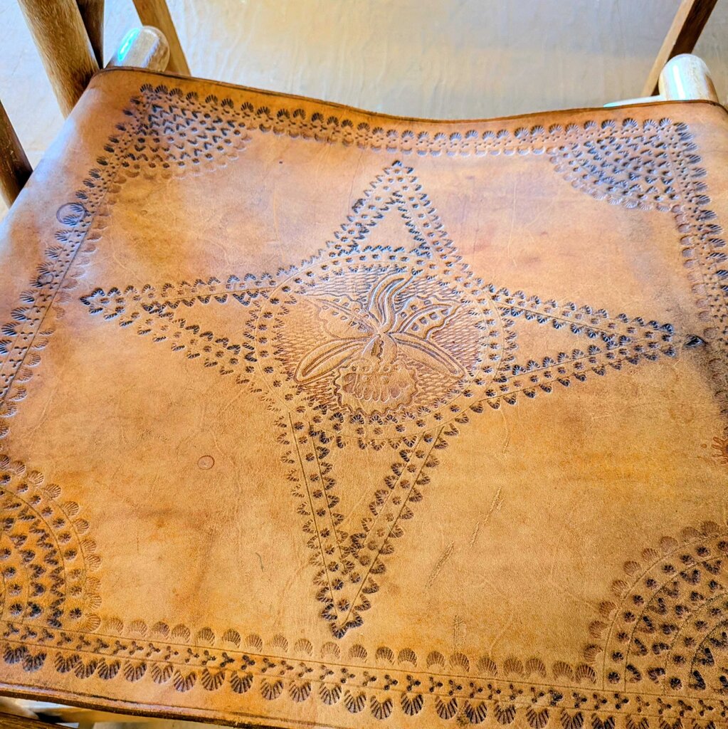 Brown leather bag with intricate embossed patterns on a wooden chair.
