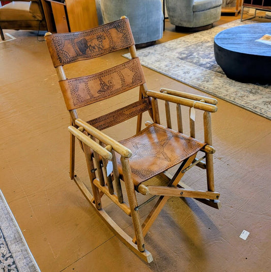 Wooden rocking chair with leather seat and backrest in a room setting.