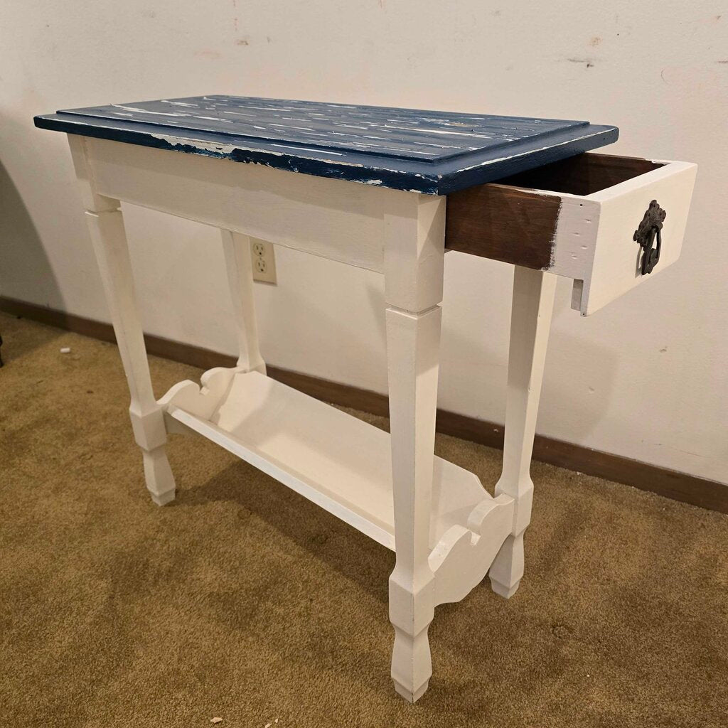 White wooden table with a blue top on a brown carpeted floor.