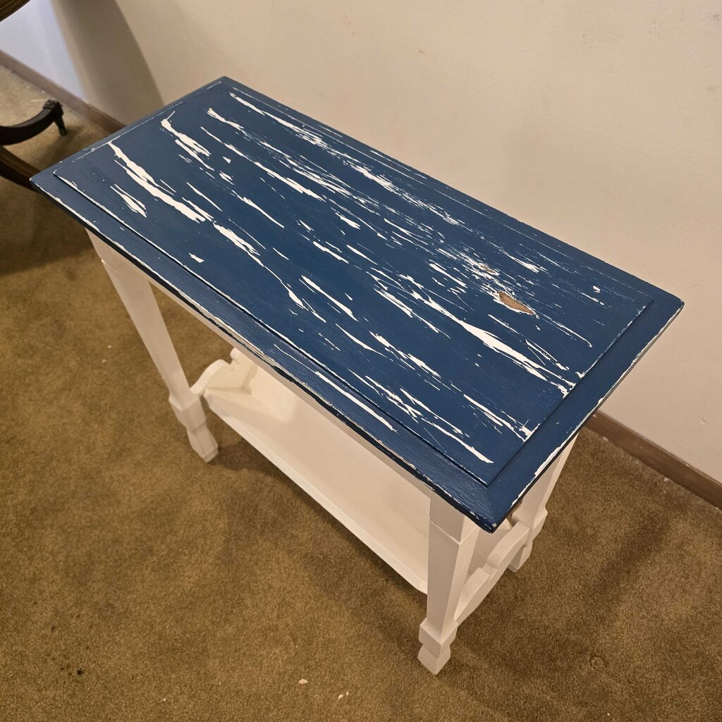 Small table with a blue distressed top and white legs on a carpeted floor.