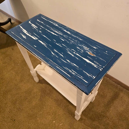 Small table with a blue distressed top and white legs on a carpeted floor.