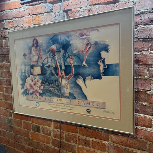 This commemorative fine art poster celebrates the 1990 Goodwill Games held in Seattle, Washington. The artwork features a dynamic multi-sport collage in a blue and earth-toned palette, depicting various athletic disciplines including basketball, cycling, figure skating, track and field, and rowing. Iconic local symbols like the Space Needle and the state of Washington are integrated into the composition.