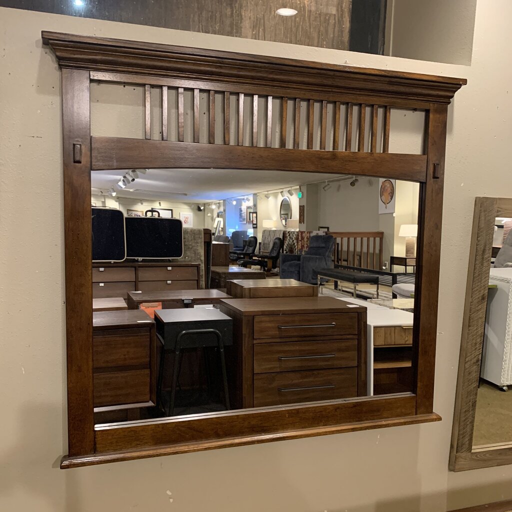 Large wooden-framed mirror reflecting an interior setting with furniture.