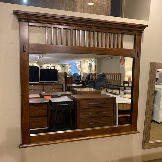 Large wooden-framed mirror reflecting an interior setting with furniture.