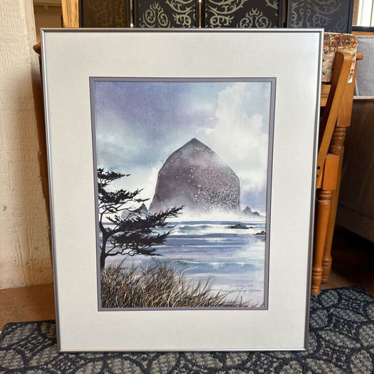 Framed artwork of a coastal scene with a large rock and ocean waves.