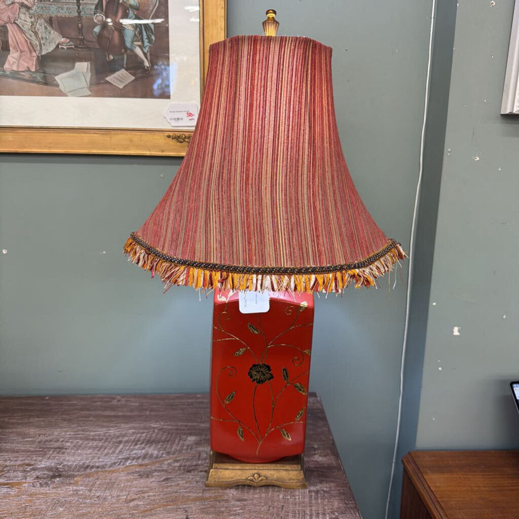 Lamp with a red and gold striped shade on a wooden base against a gray wall.