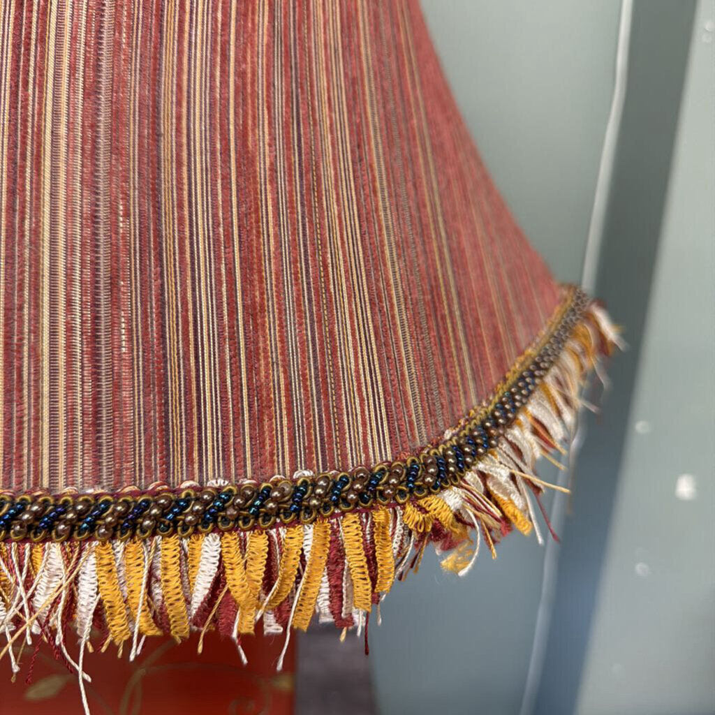 Close-up of a textured fabric with fringes and a colorful trim against a neutral background