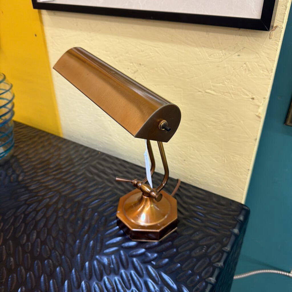 Vintage-style brass desk lamp on a textured surface with a yellow wall in the background.