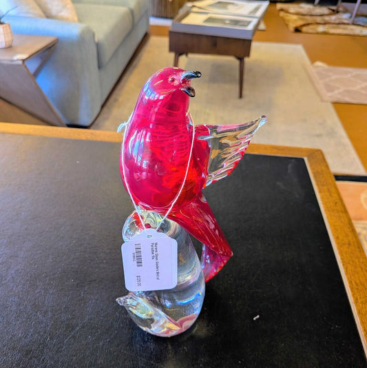 Glass bird figurine with a tag on a dark surface, indoor setting