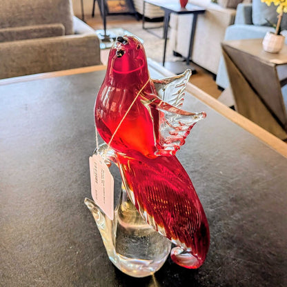 Red glass bird figurine on a table with a blurred indoor setting