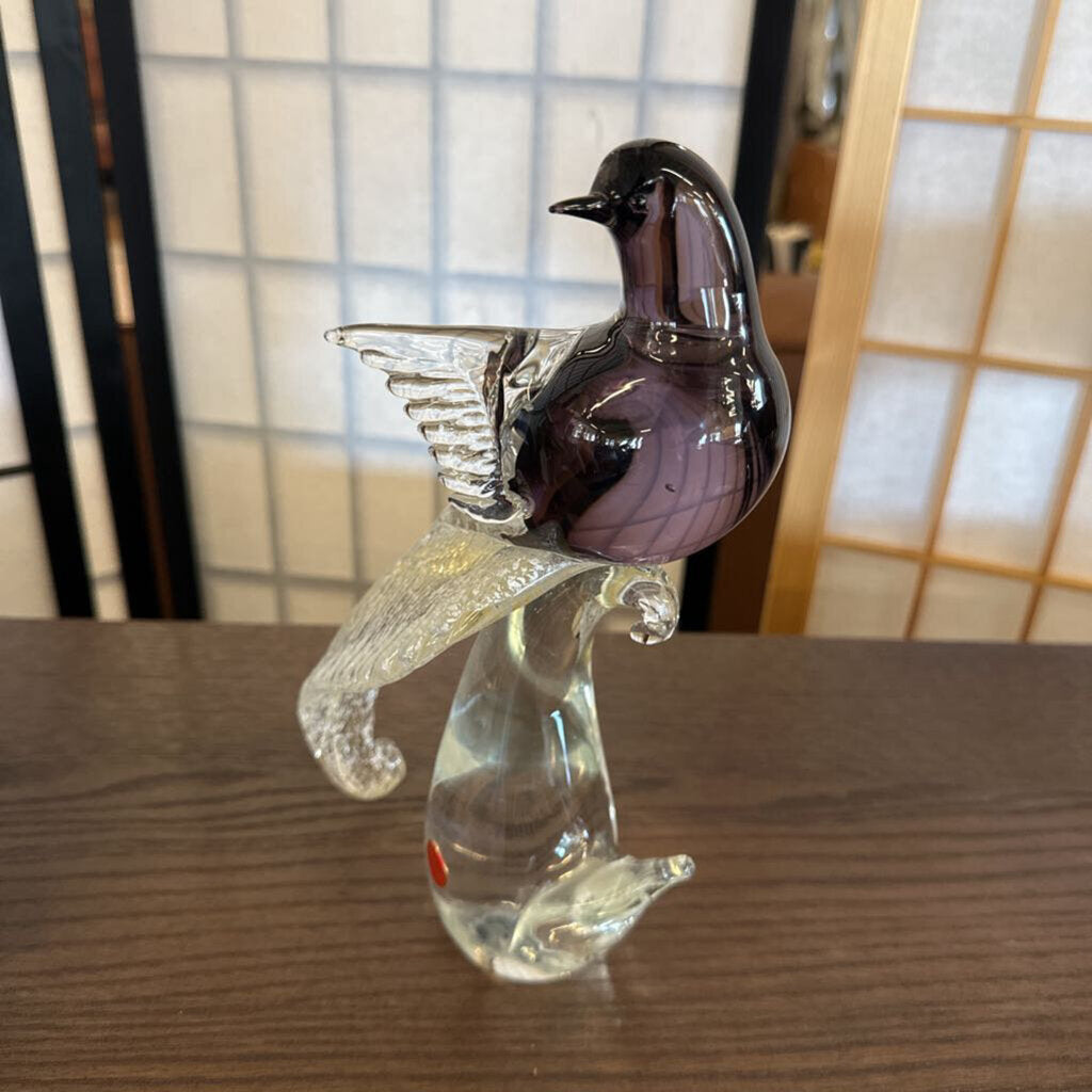 Glass sculpture of a bird perched on a branch on a wooden surface