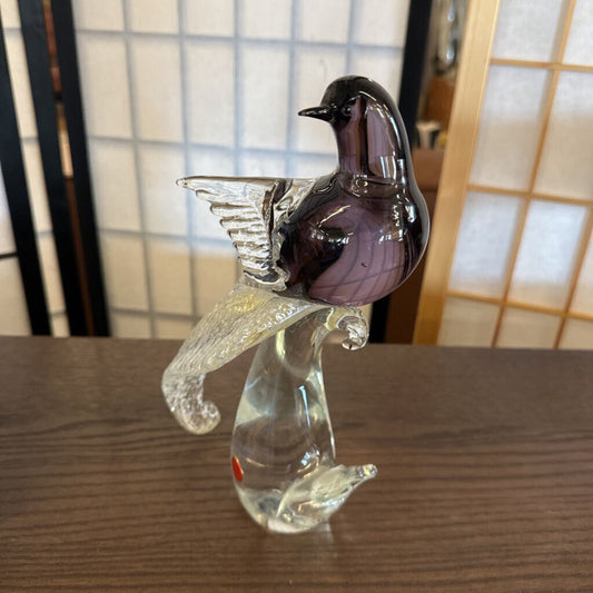 Glass sculpture of a bird perched on a branch on a wooden surface