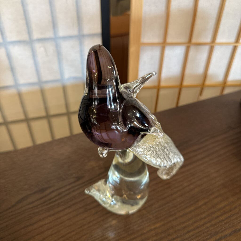 Glass sculpture of a bird on a wooden surface with a tiled wall background