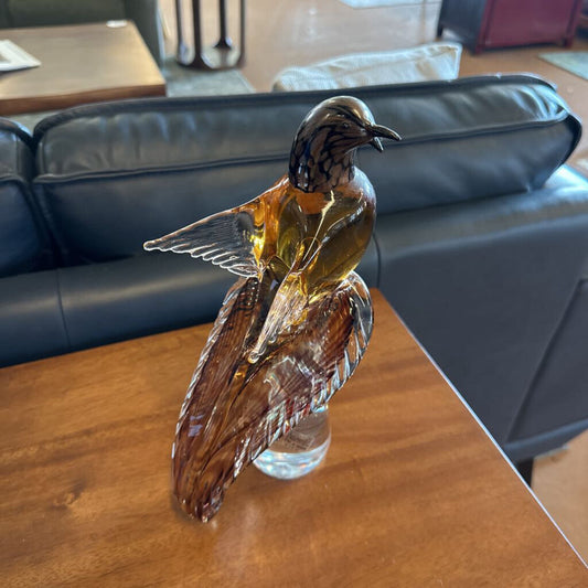 Decorative glass bird sculpture on a wooden table with a blue sofa in the background