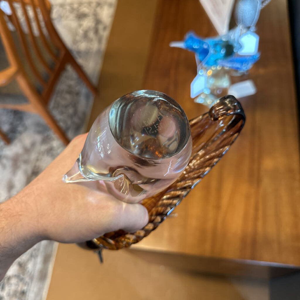 Clear glass object held by a hand with a wooden chair and table in the background