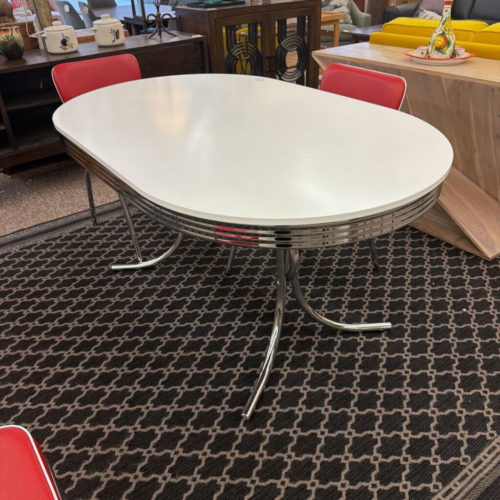 Modern dining table with a white top and chrome base on a patterned rug.