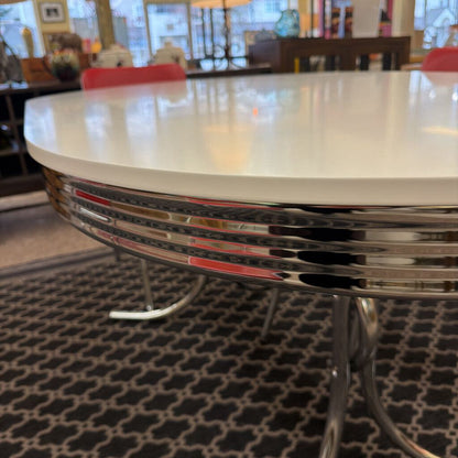 Round metal table with a white top in a room with chairs and a rug.