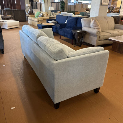 Gray sofa in a furniture store with other sofas and tables in the background.
